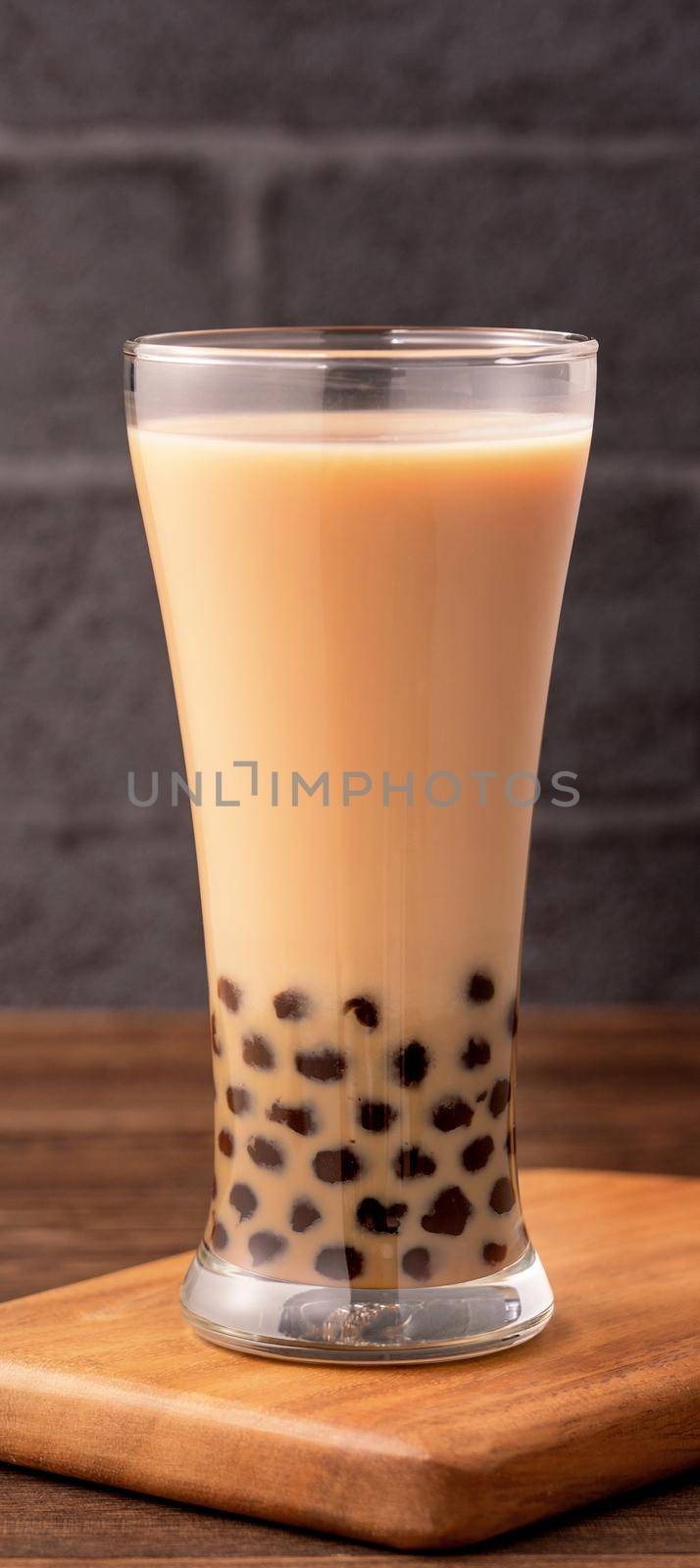 Delicious bubble milk tea with tapioca pearl ball in glass on wooden table and dark gray brick background, popular food and drink in Taiwan, close up by ROMIXIMAGE