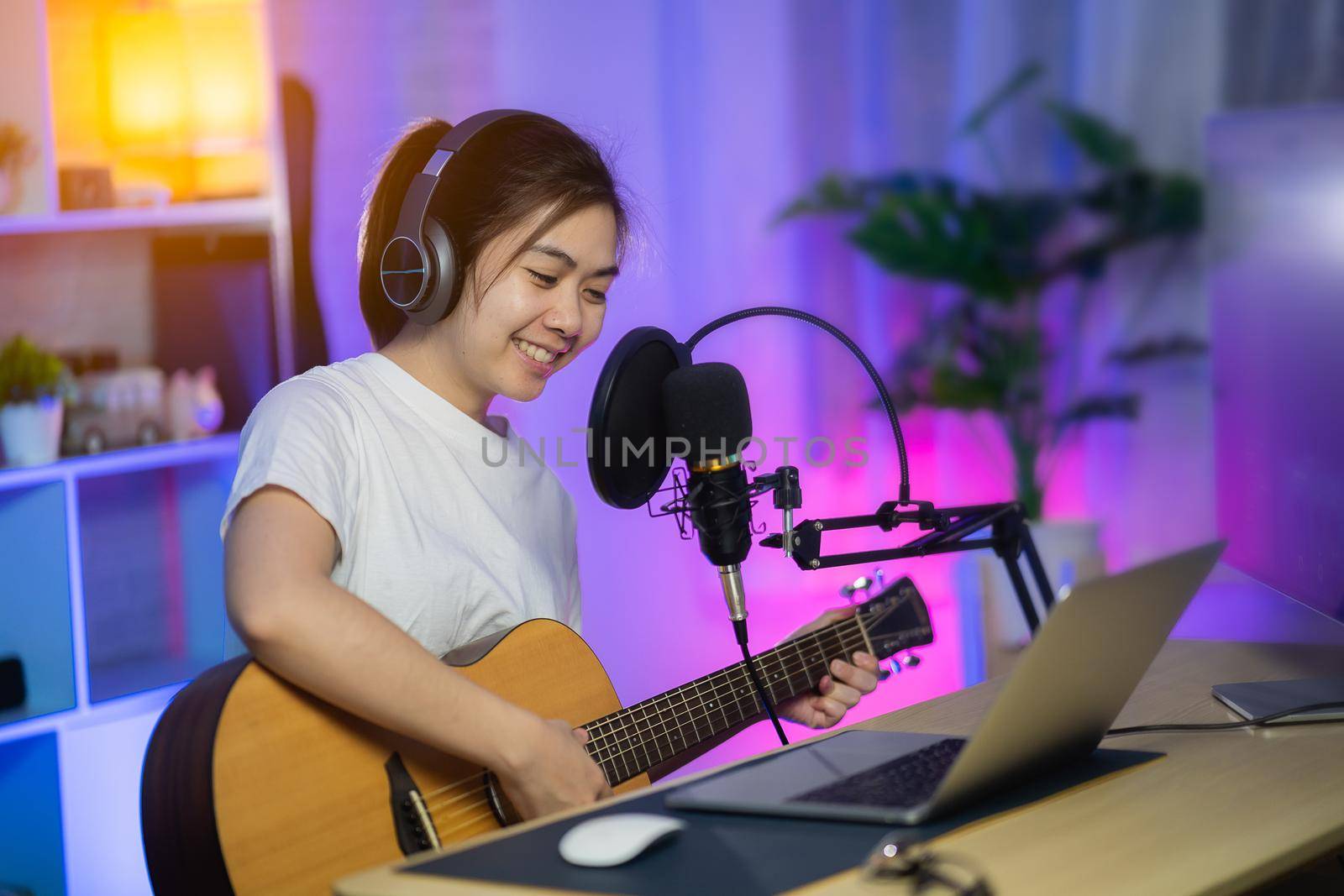 Beautiful girl singing with headphone and playing guitar recording new song with microphone in the home recording studio by Wmpix