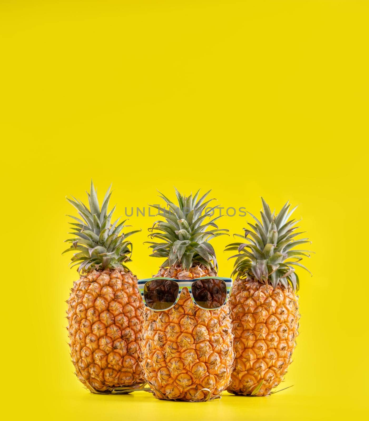 Creative pineapples with sunglasses isolated on yellow background, summer vacation beach idea design pattern, copy space, close up, blank for text by ROMIXIMAGE