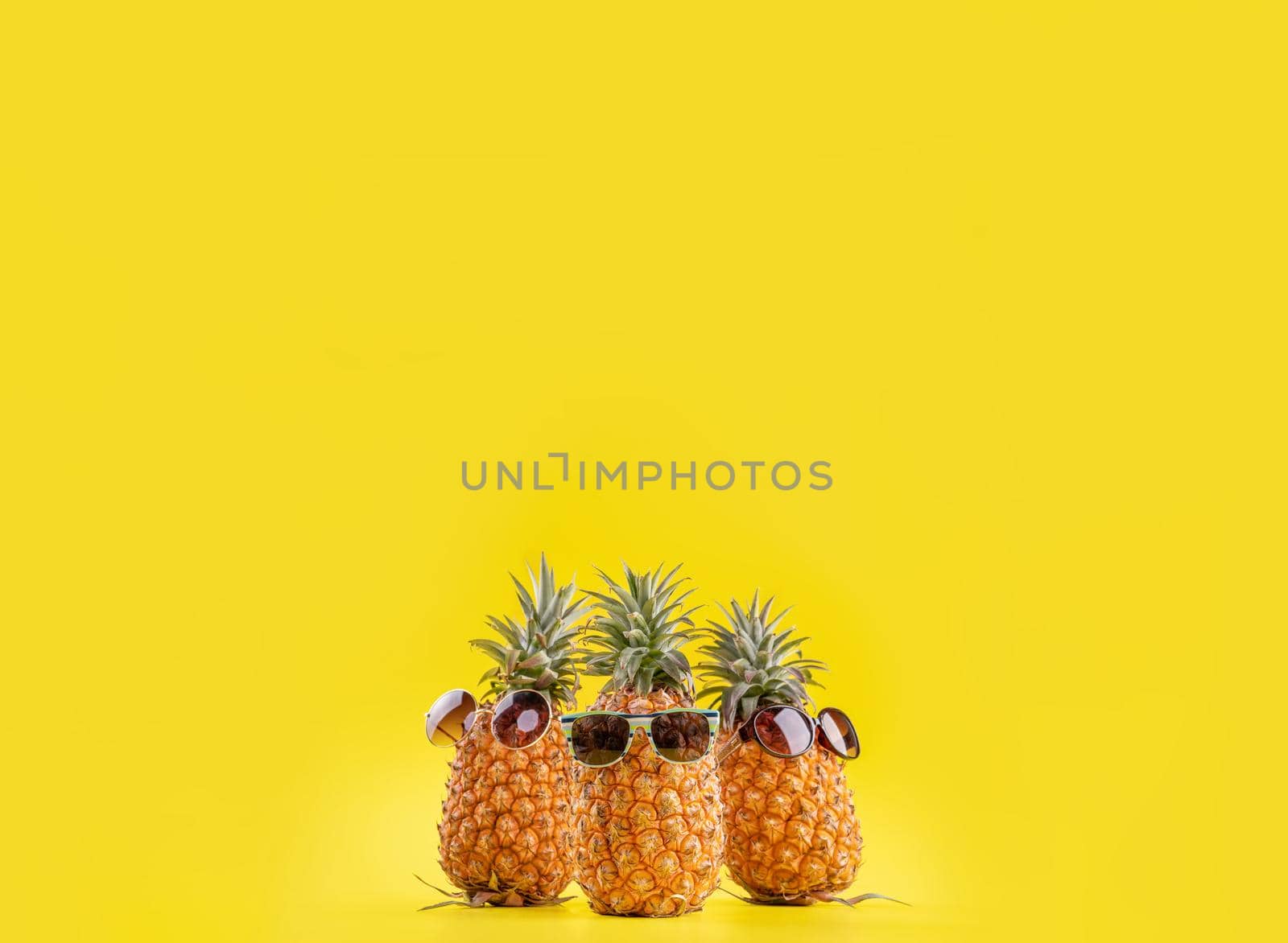 Creative pineapples with sunglasses isolated on yellow background, summer vacation beach idea design pattern, copy space, close up, blank for text by ROMIXIMAGE