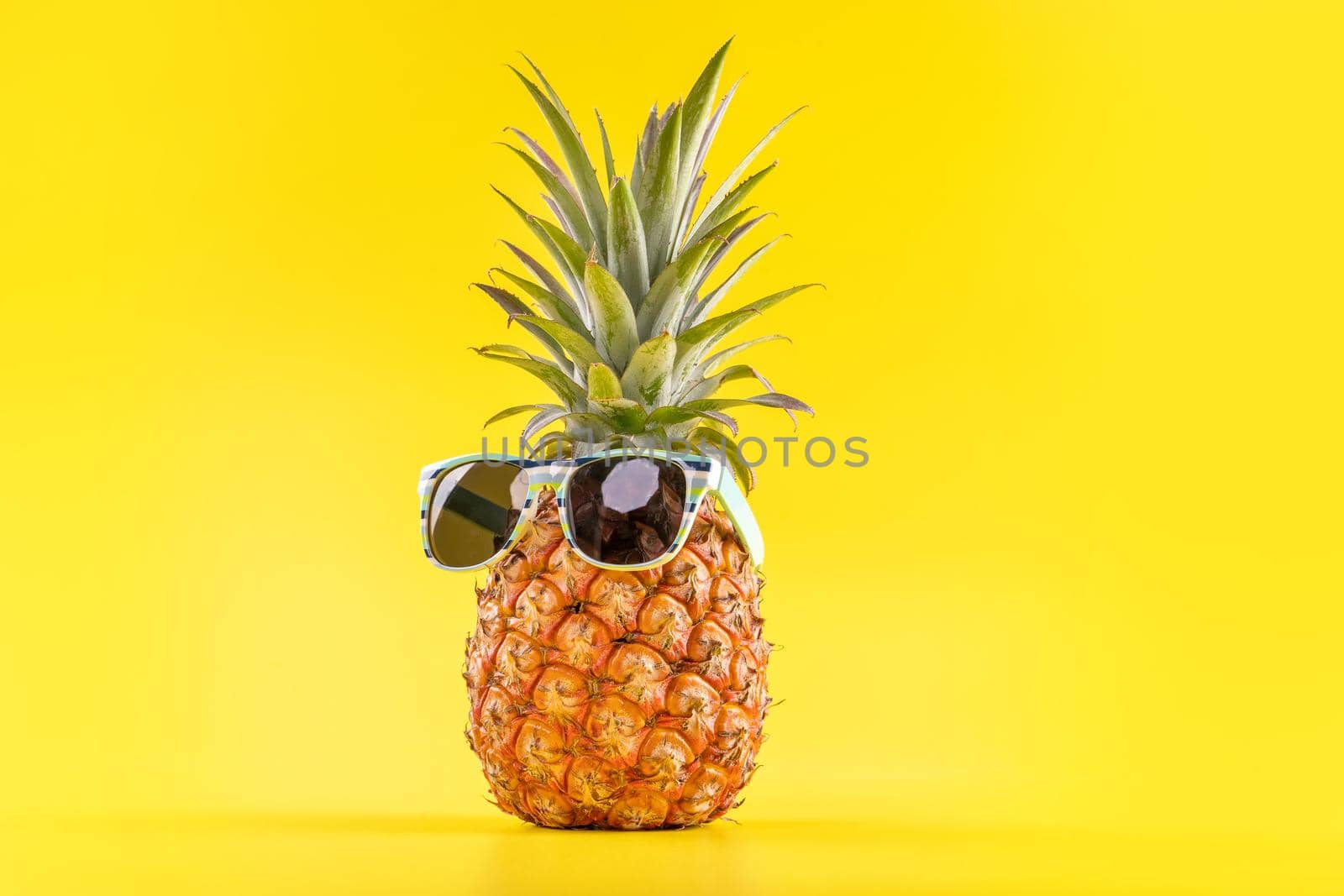 Creative pineapples with sunglasses isolated on yellow background, summer vacation beach idea design pattern, copy space, close up, blank for text by ROMIXIMAGE