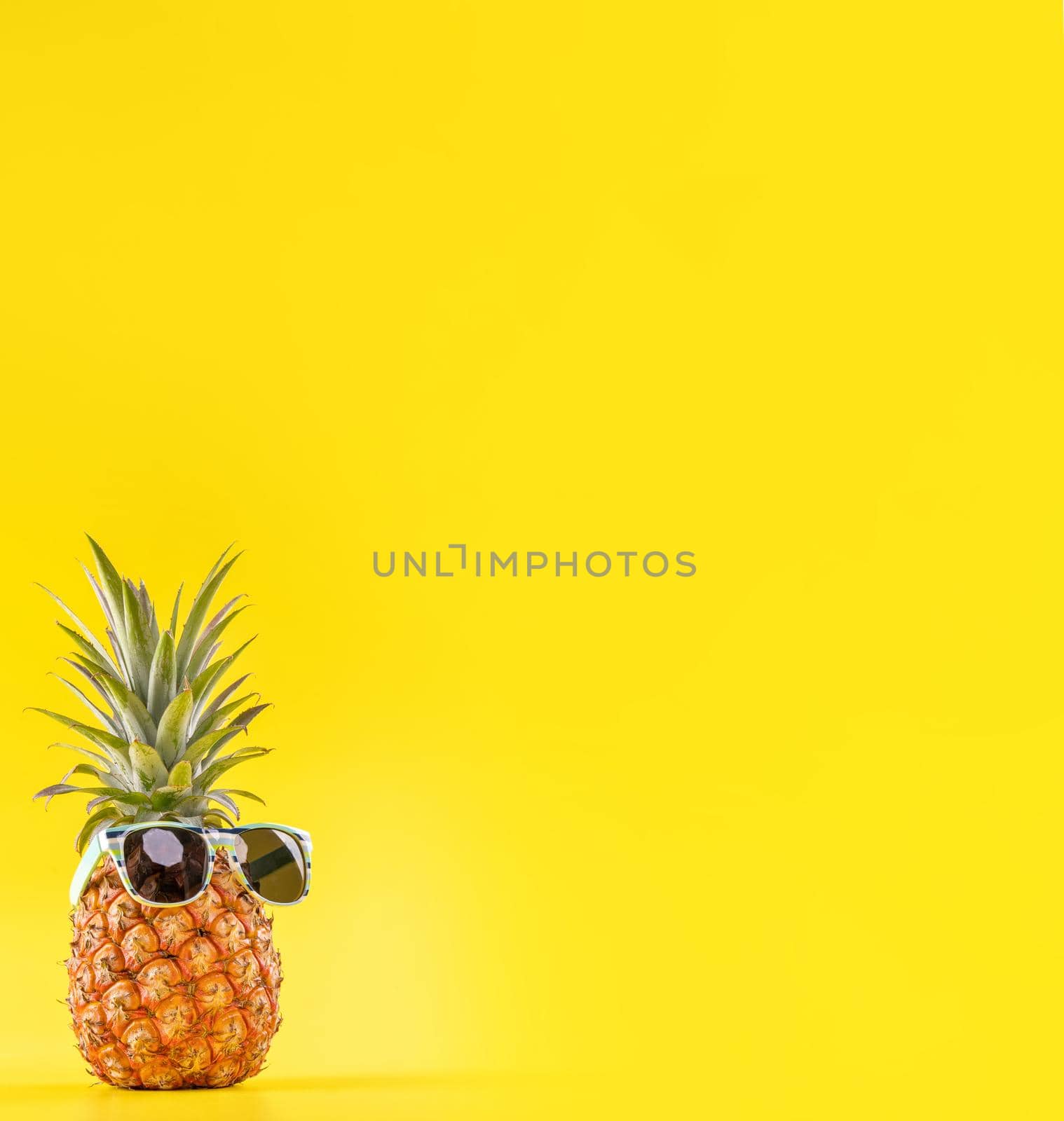 Creative pineapple looking up with sunglasses and shell isolated on yellow background, summer vacation beach idea design pattern, copy space close up by ROMIXIMAGE