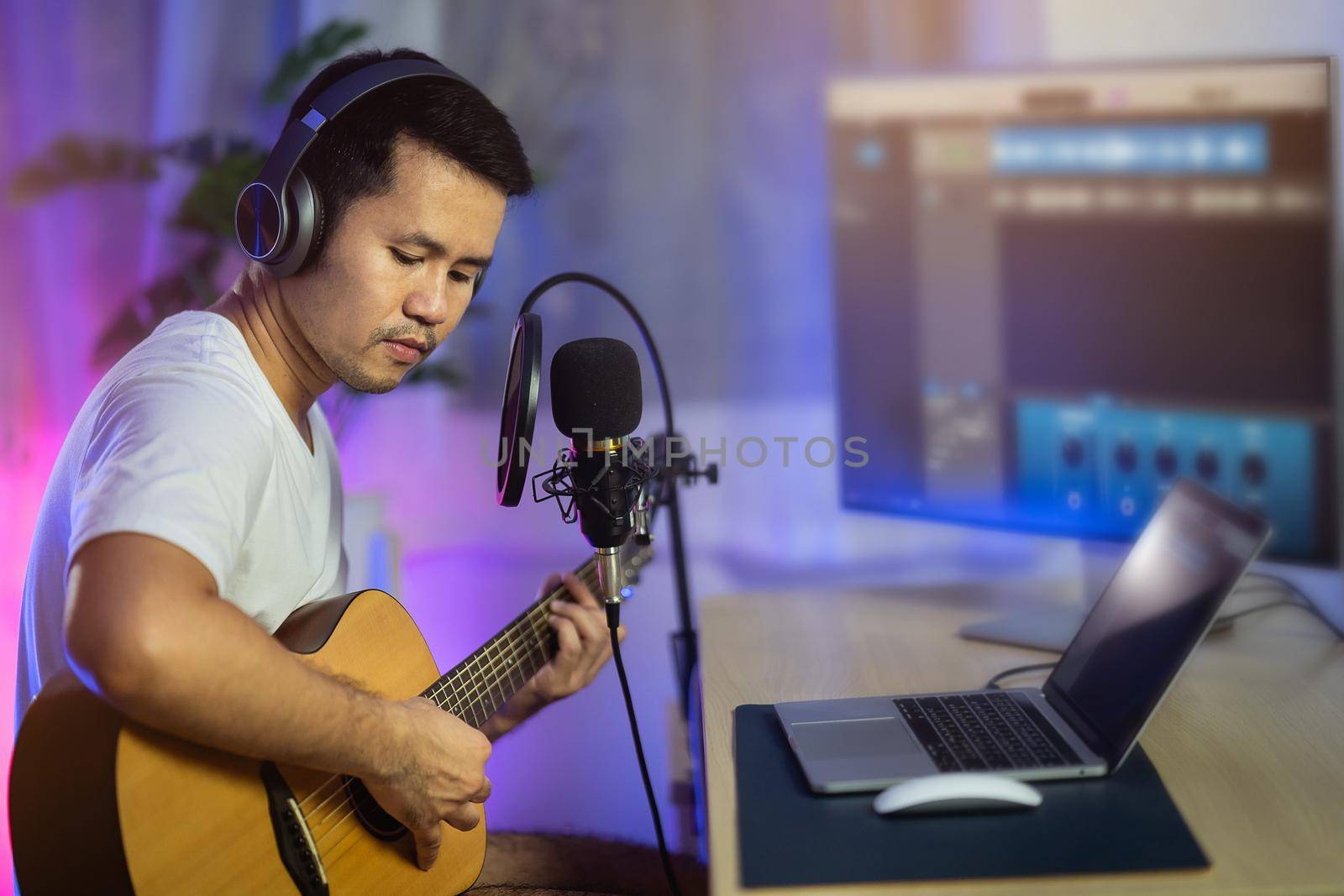 Man singing with headphone and playing guitar recording new song with microphone in the home recording studio