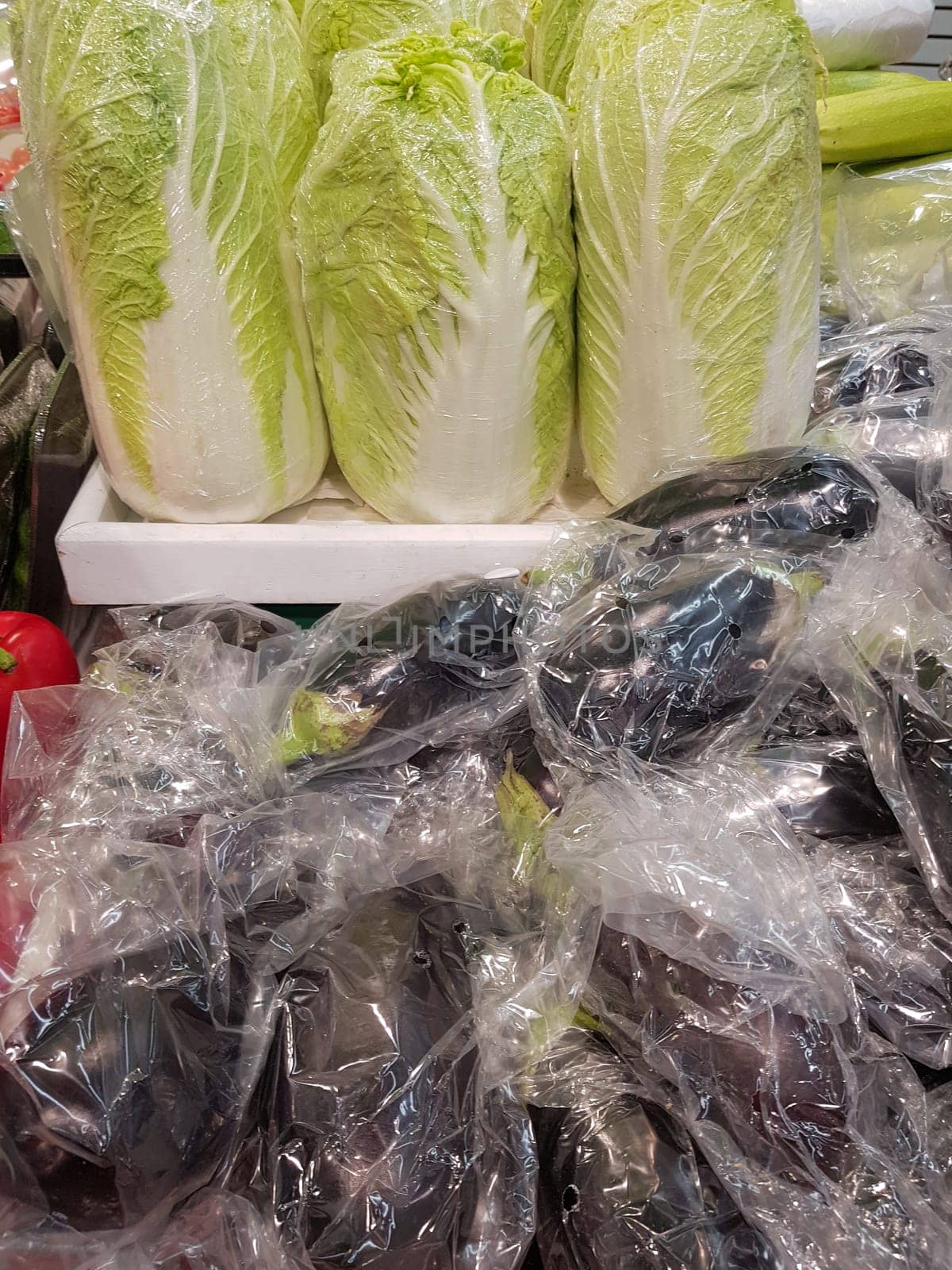 A lot of Chinese cabbage and eggplant in plastic bags on the counter of the vegetable market, vertical.