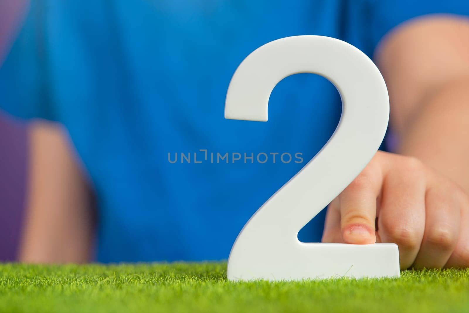 White number 2 in hand. The hand holding the number 2 symbolizes choice, partnership and duality, the choice between two alternatives, to combine the efforts of two people to achieve a common goal. by SERSOL