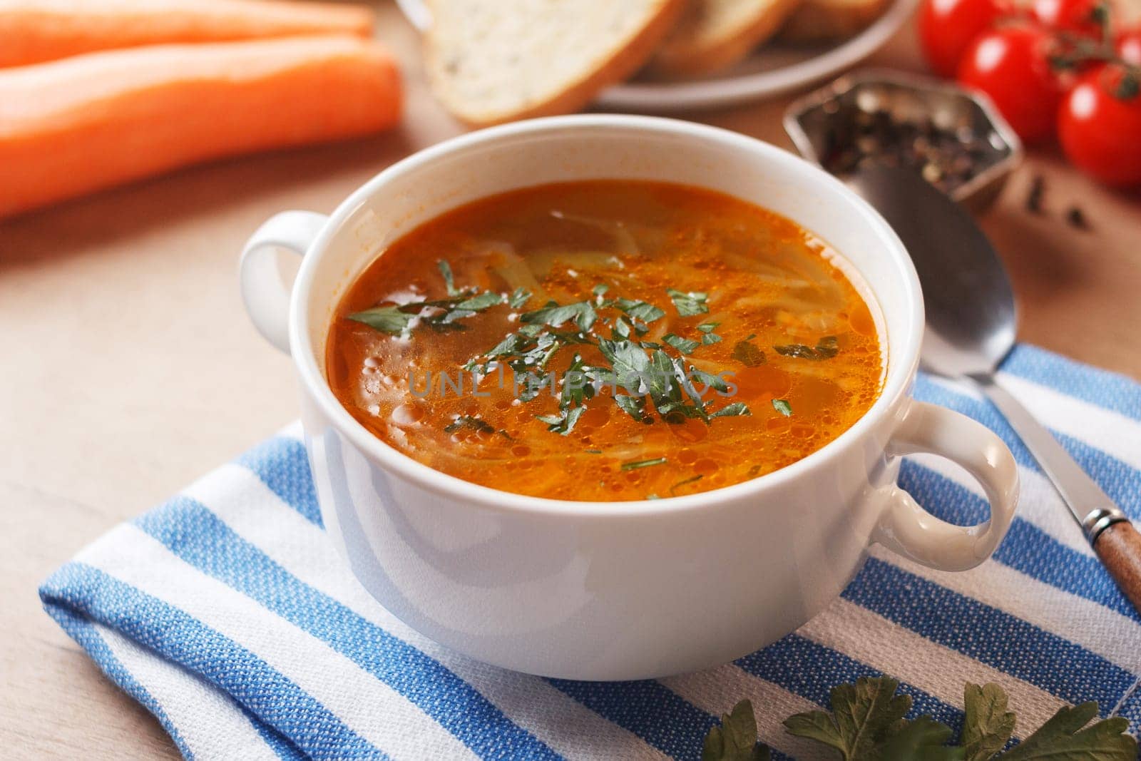 Vegetable soup with potatoes, cabbage, carrots and onions in a white bowl on the kitchen table. Vegetarian food.