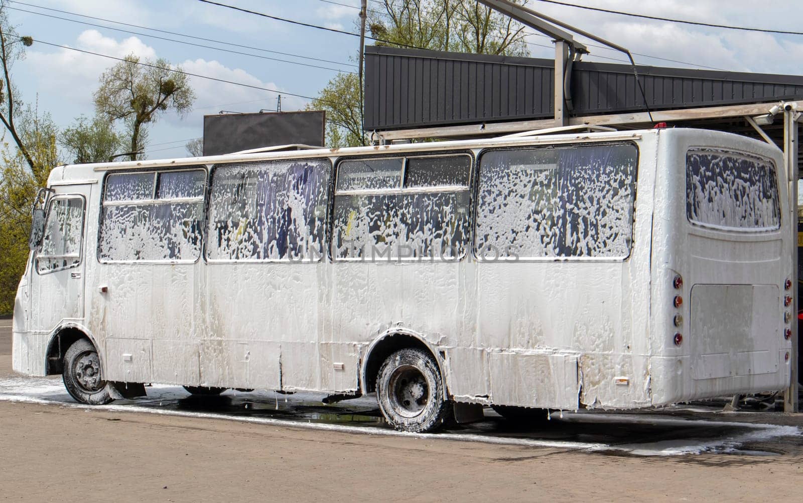 Big white bus in foam at a self-service car wash. External washing of public transport buses. Self-service manual high-pressure car wash in the open air