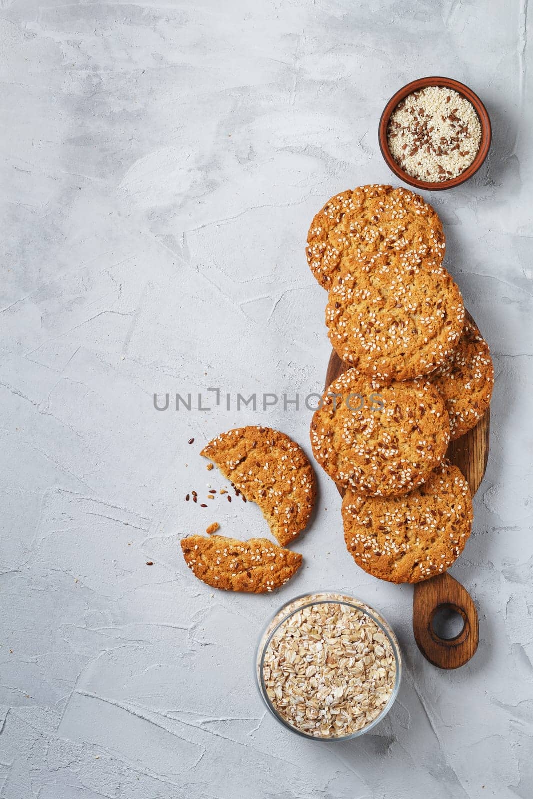 Oatmeal cookies with sesame seeds and flax seeds on a gray background with a jar of oatmeal and textiles. copy space