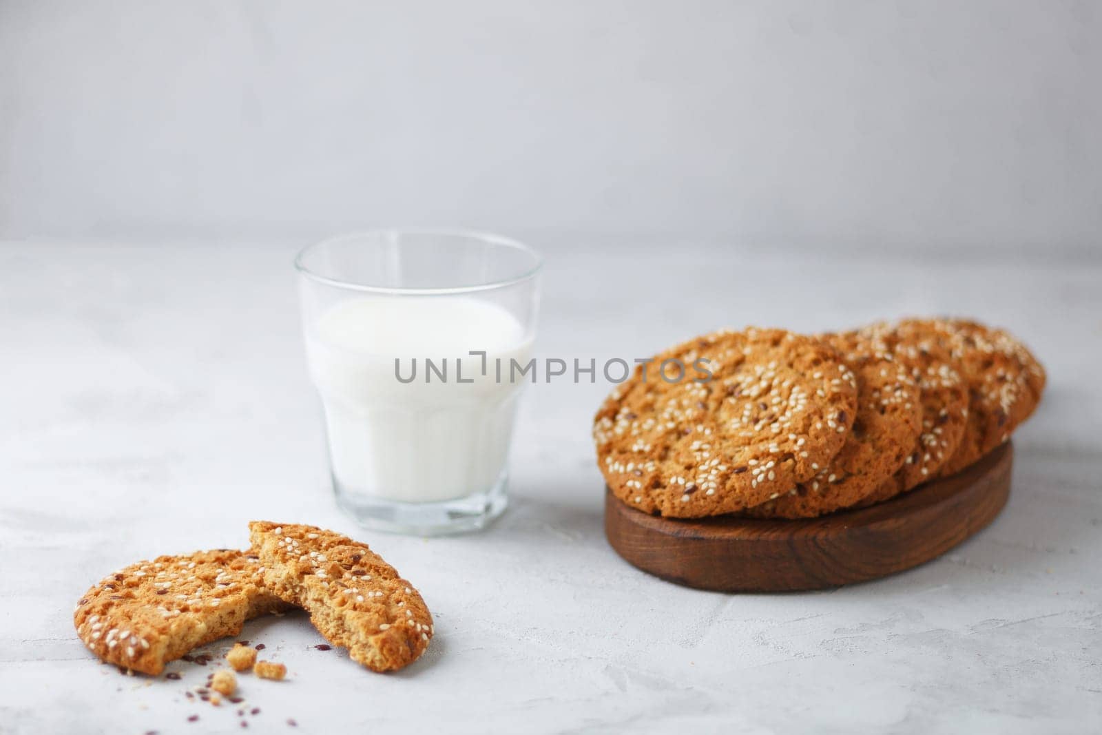 Oatmeal cookies with sesame seeds and flax seeds with a glass of milk on a gray background.Copy space