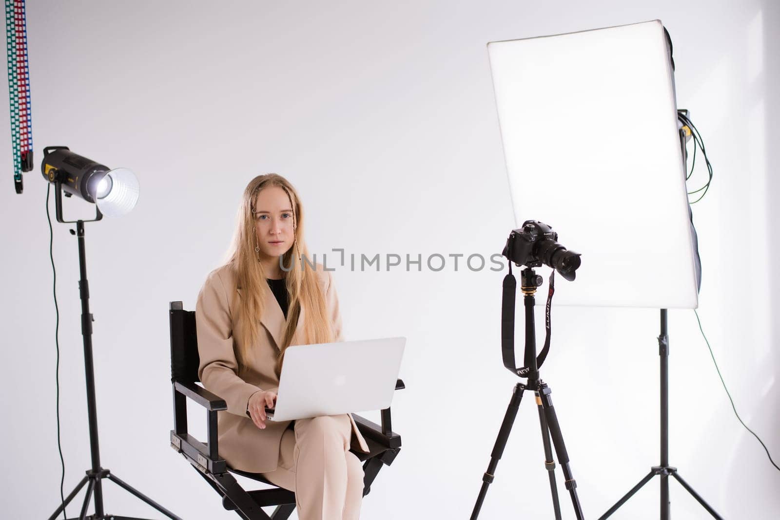 A business woman videographer producer assistant in a suit is working, typing on a laptop and sitting on a chair. Video Production studio, tripod camera