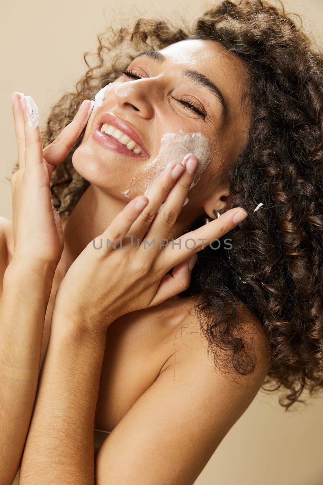 Woman beauty face close-up applying foam to wash and cleanse skin with fingers of her hand, nail and hair health, hair dryer style curly afro hair, body and beauty care concept. High quality photo