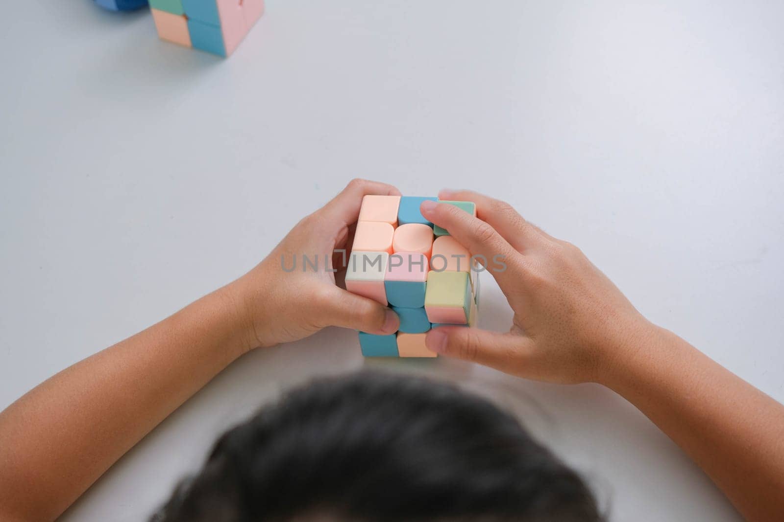 Asian little cute girl holding Rubik's cube in her hands and playing with it. Rubik's cube is a game that increases intelligence for children. Educational toys for children by TEERASAK