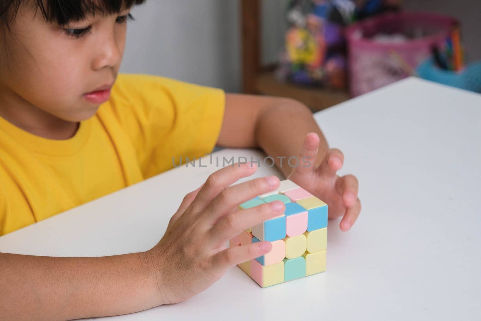 Asian little cute girl holding Rubik's cube in her hands and playing with it. Rubik's cube is a game that increases intelligence for children. Educational toys for children by TEERASAK