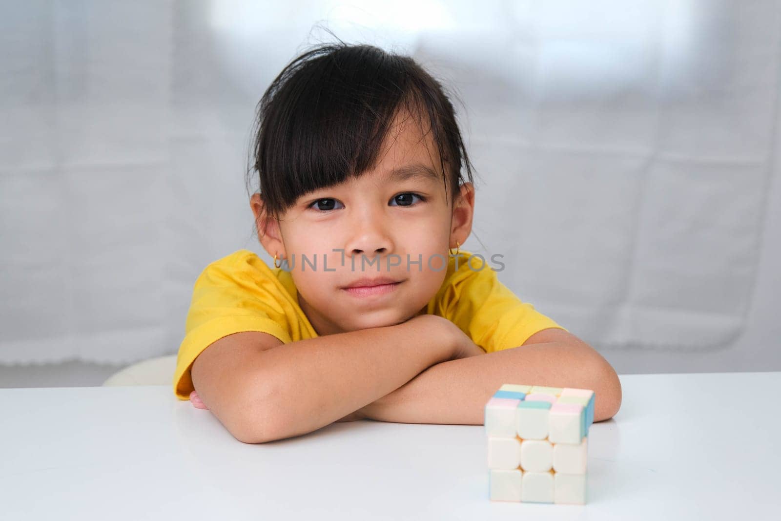 Asian little cute girl holding Rubik's cube in her hands and playing with it. Rubik's cube is a game that increases intelligence for children. Educational toys for children by TEERASAK