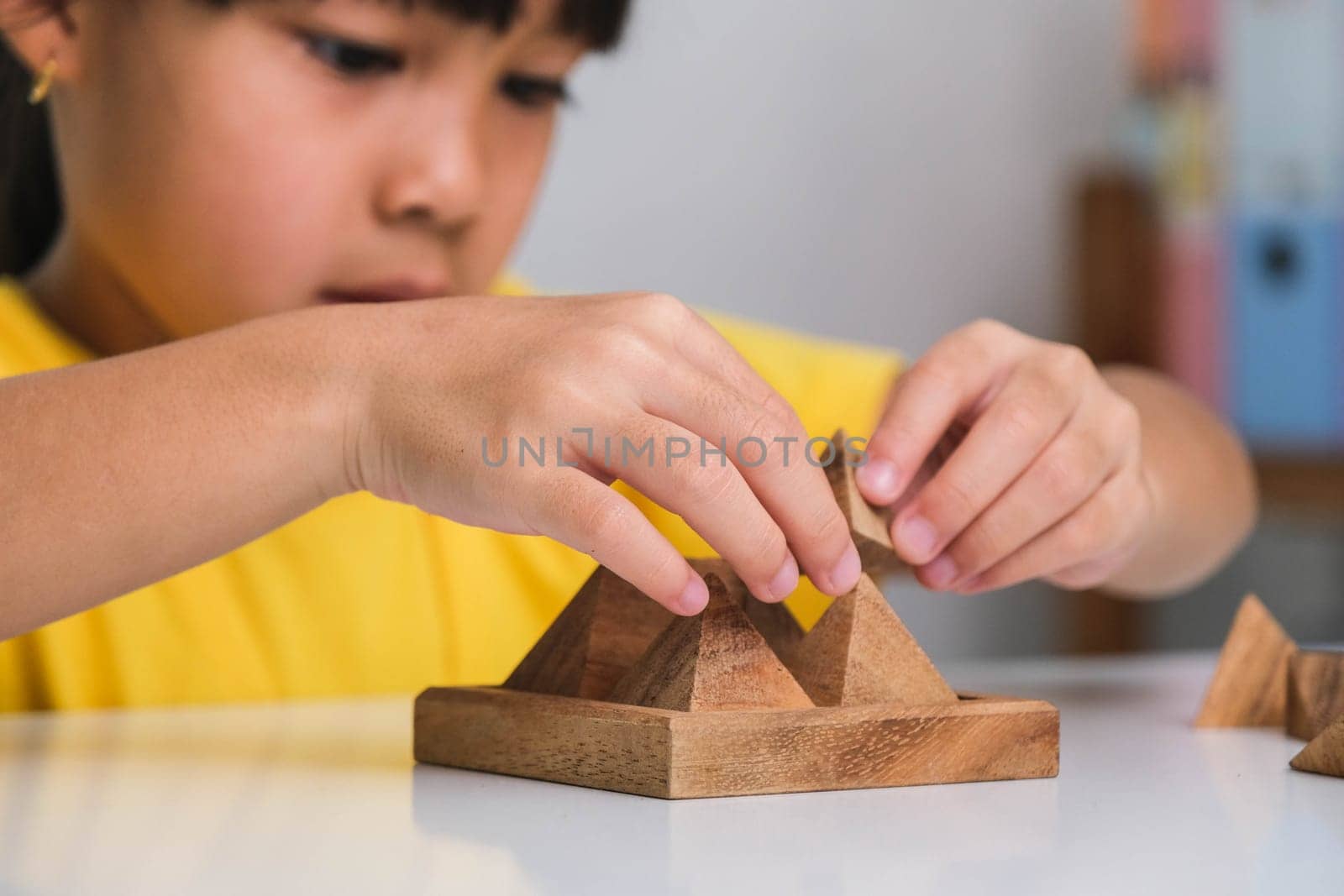 Asian cute little girl playing with wooden toy jigsaw puzzle pyramid on table. Healthy children training memory and thinking. Wooden puzzles are games that increase intelligence for children. Educational toys for children.