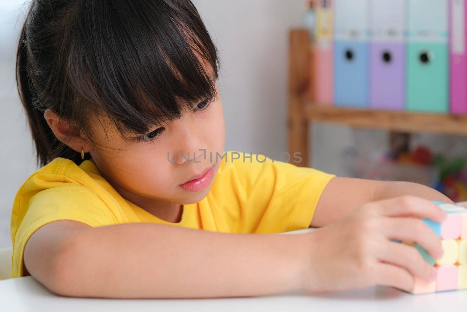 Asian little cute girl holding Rubik's cube in her hands and playing with it. Rubik's cube is a game that increases intelligence for children. Educational toys for children by TEERASAK