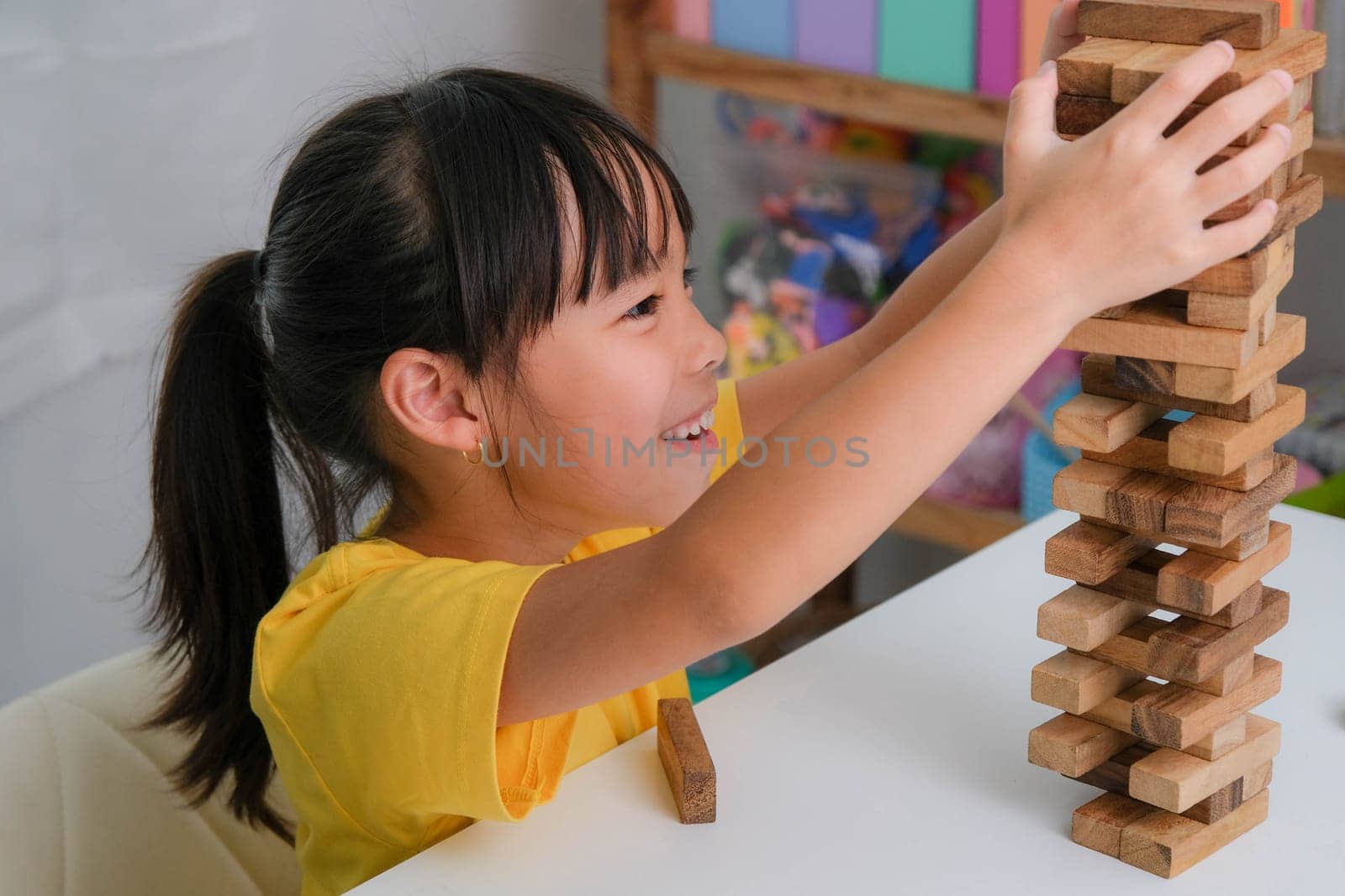 Cute Asian siblings having fun playing Jenga together. Two children playing Jenga board game on table in room at home. Wooden puzzles are games that increase intelligence for children. Educational toys for children.