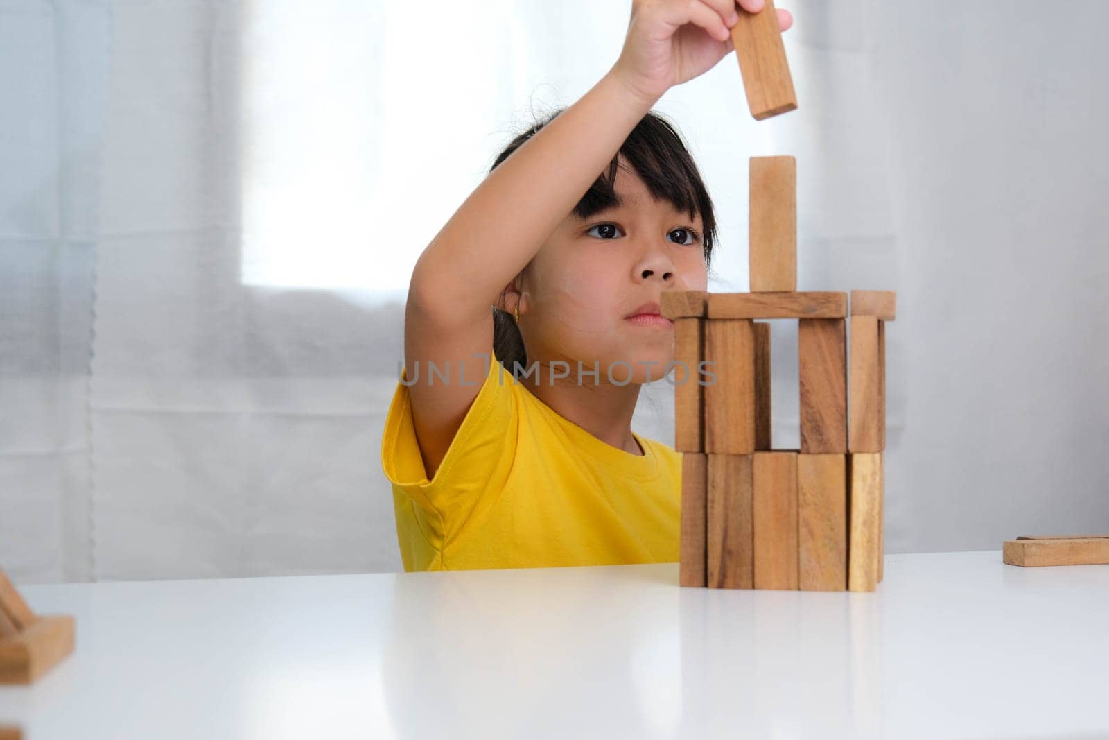 Asian cute little girl playing with constructor wooden block building. Healthy children training memory and thinking. Wooden puzzles are games that increase intelligence for children. Educational toys for children. by TEERASAK