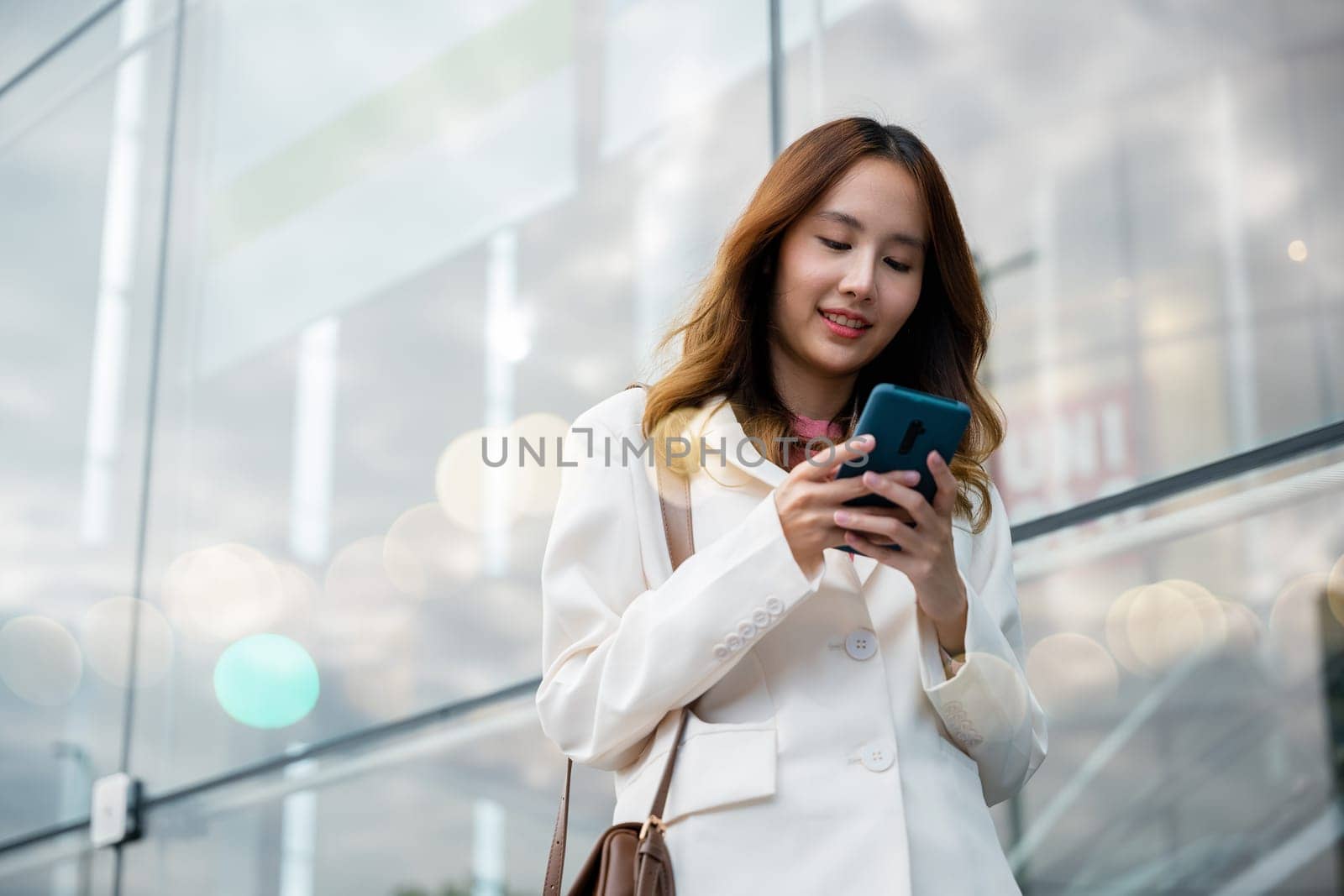 Portrait successful business woman smiling holding smartphone using app chat online in morning, Asian businesswoman typing text on mobile phone standing outdoors street front building near office