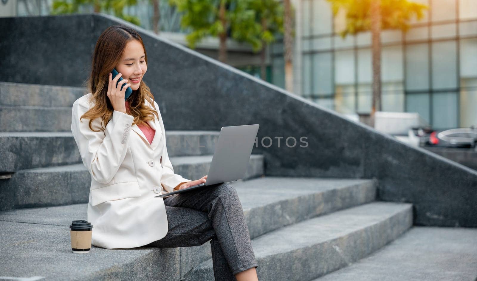 Asian woman freelance looking laptop with smile while talking on mobile smartphone by Sorapop