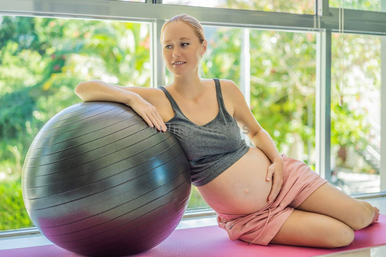 Pregnant woman exercising on fitball at home. Pregnant woman doing relax exercises with a fitness pilates ball. Against the background of the window.