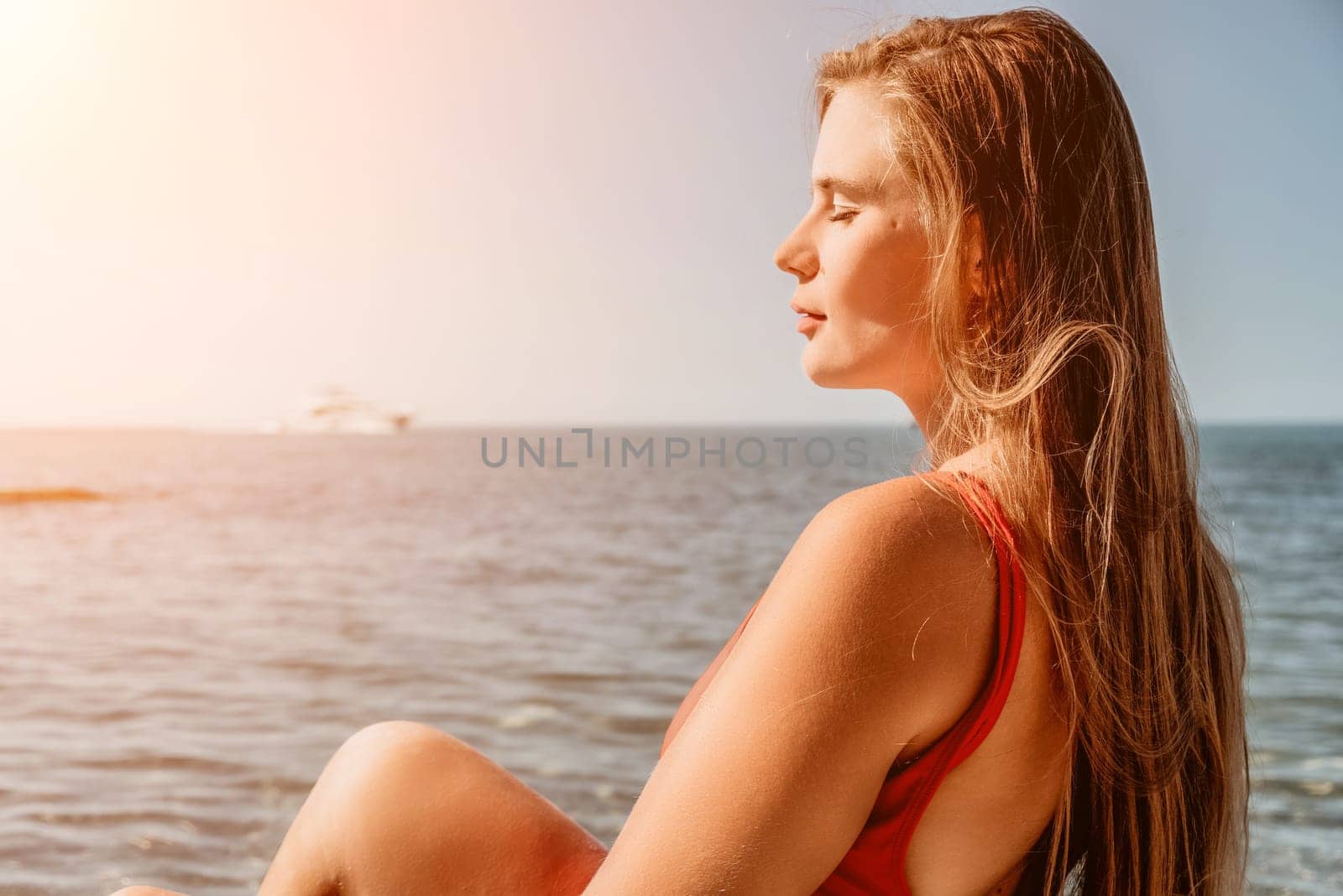 Young woman in red bikini on Beach. Girl lying on pebble beach and enjoying sun. Happy lady with long hair in bathing suit chilling and sunbathing by turquoise sea ocean on hot summer day. Close up by panophotograph