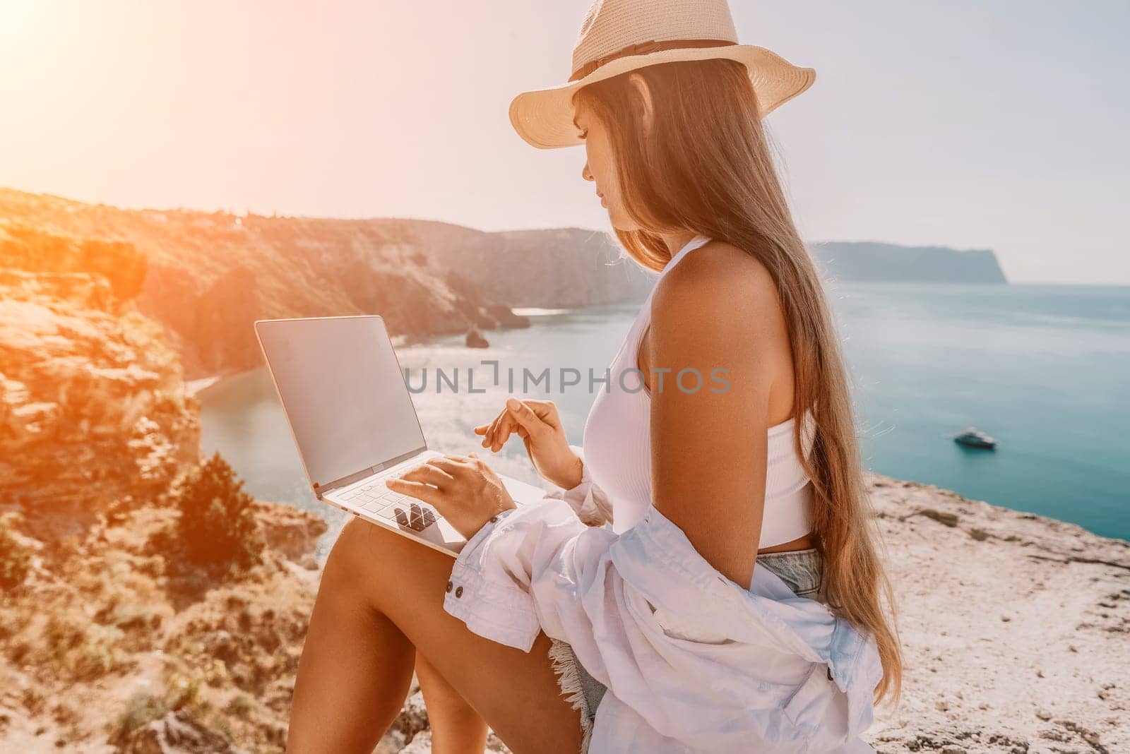 Digital nomad, Business woman working on laptop by the sea. Pretty lady typing on computer by the sea at sunset, makes a business transaction online from a distance. Freelance remote work on vacation