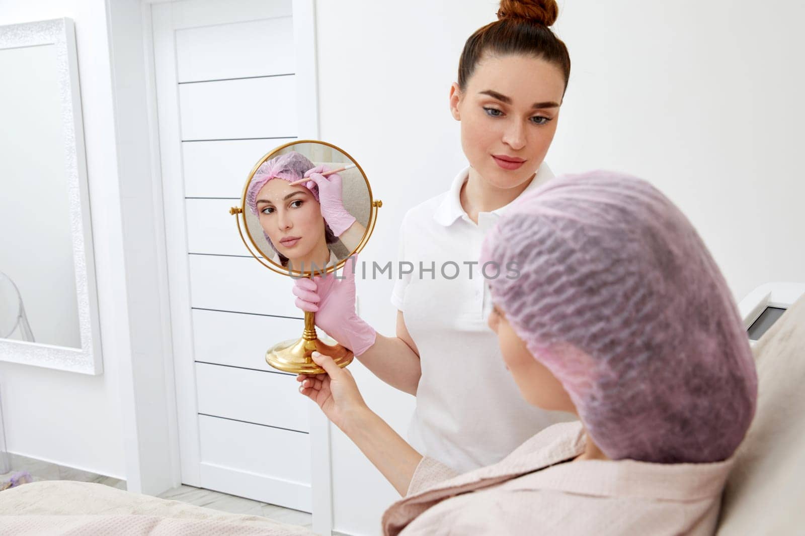 Young woman sitting in medical chair and looking in the mirror. She is satisfied after successful beauty treatment by Mariakray