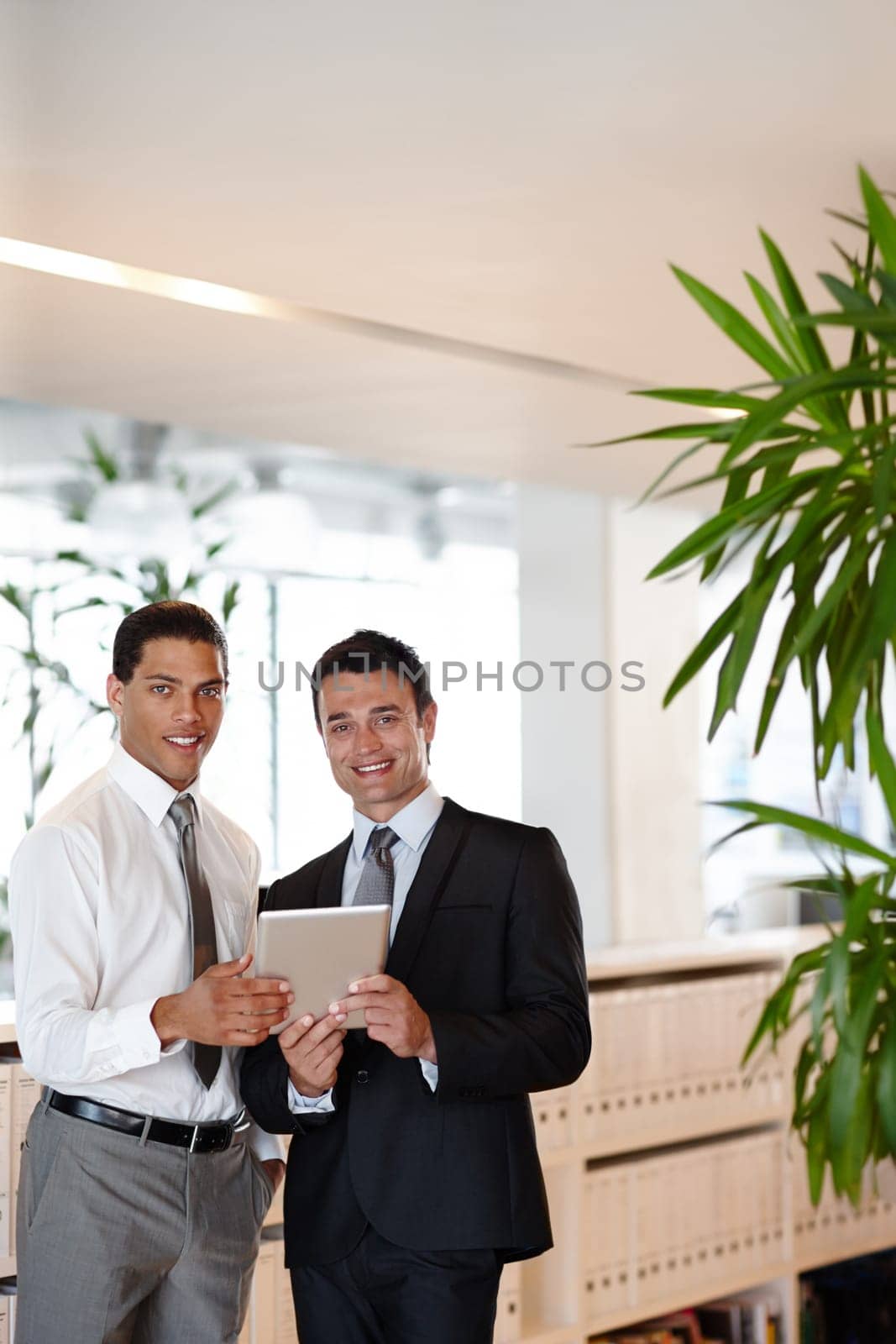 Using technology to enhance their business. Two suit-clad businessmen working together while in the office