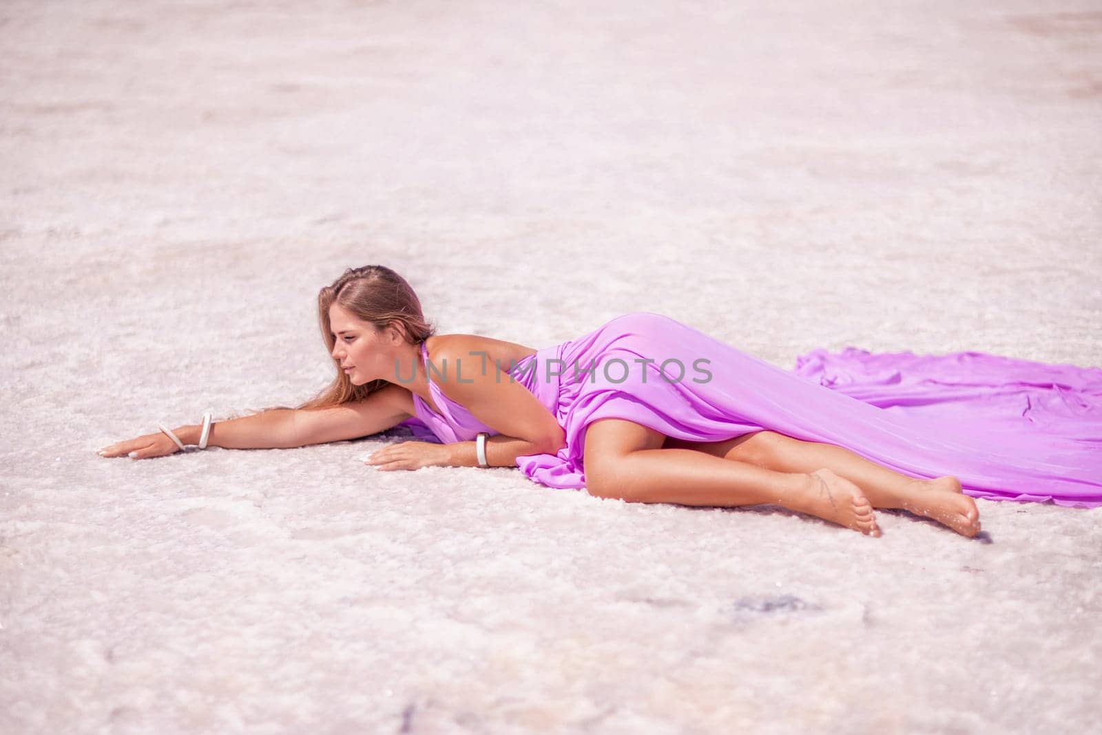 A woman in a pink dress lies on the shore of a pink lake, takes a photo for memory and leaves unforgettable memories