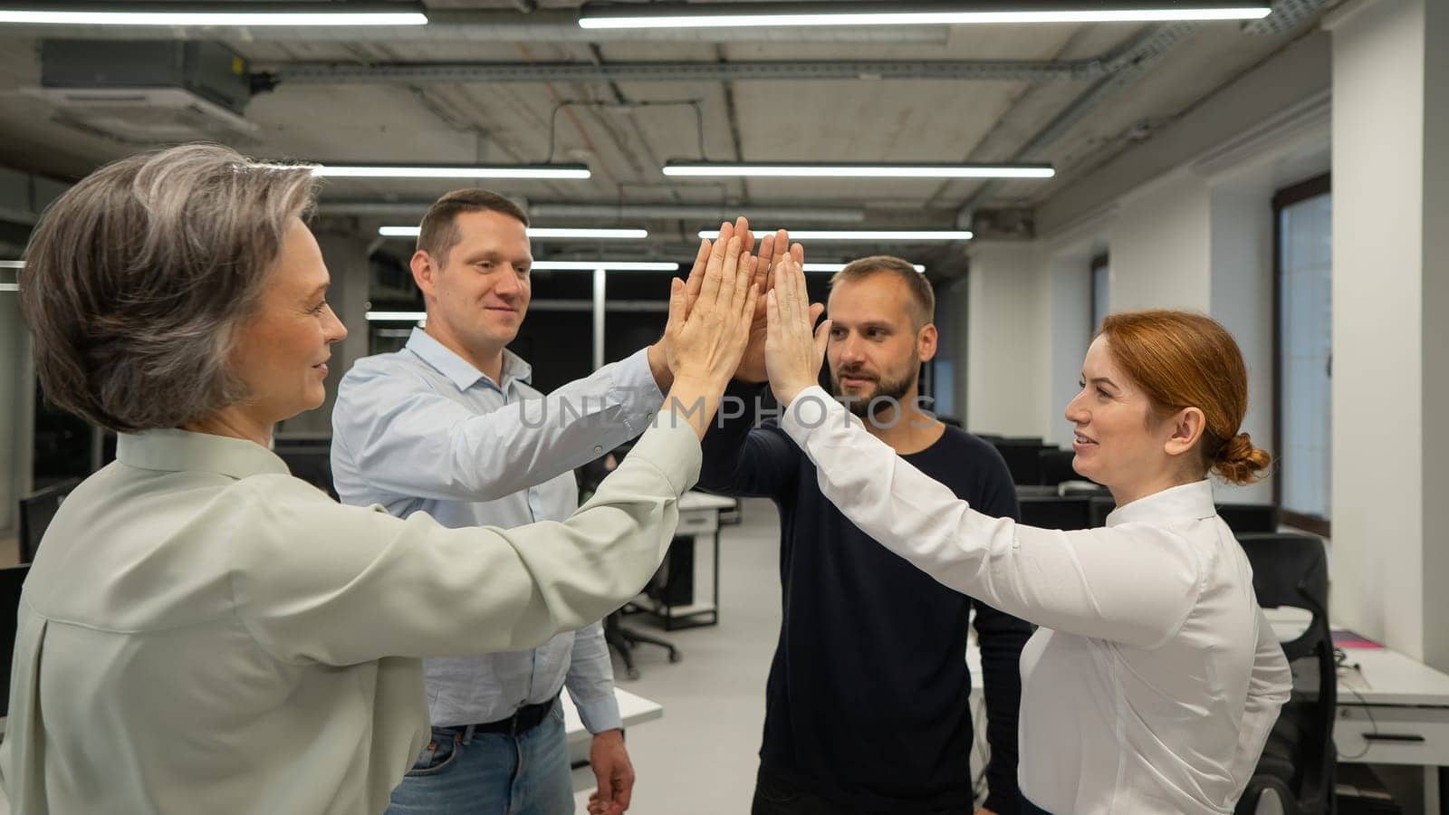 Four co-workers give a high five in the office. by mrwed54