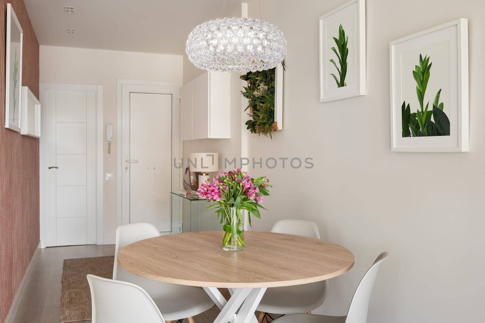 Entrance hall dining room with a round wooden table, white chairs and paintings in the interior of a modern apartment