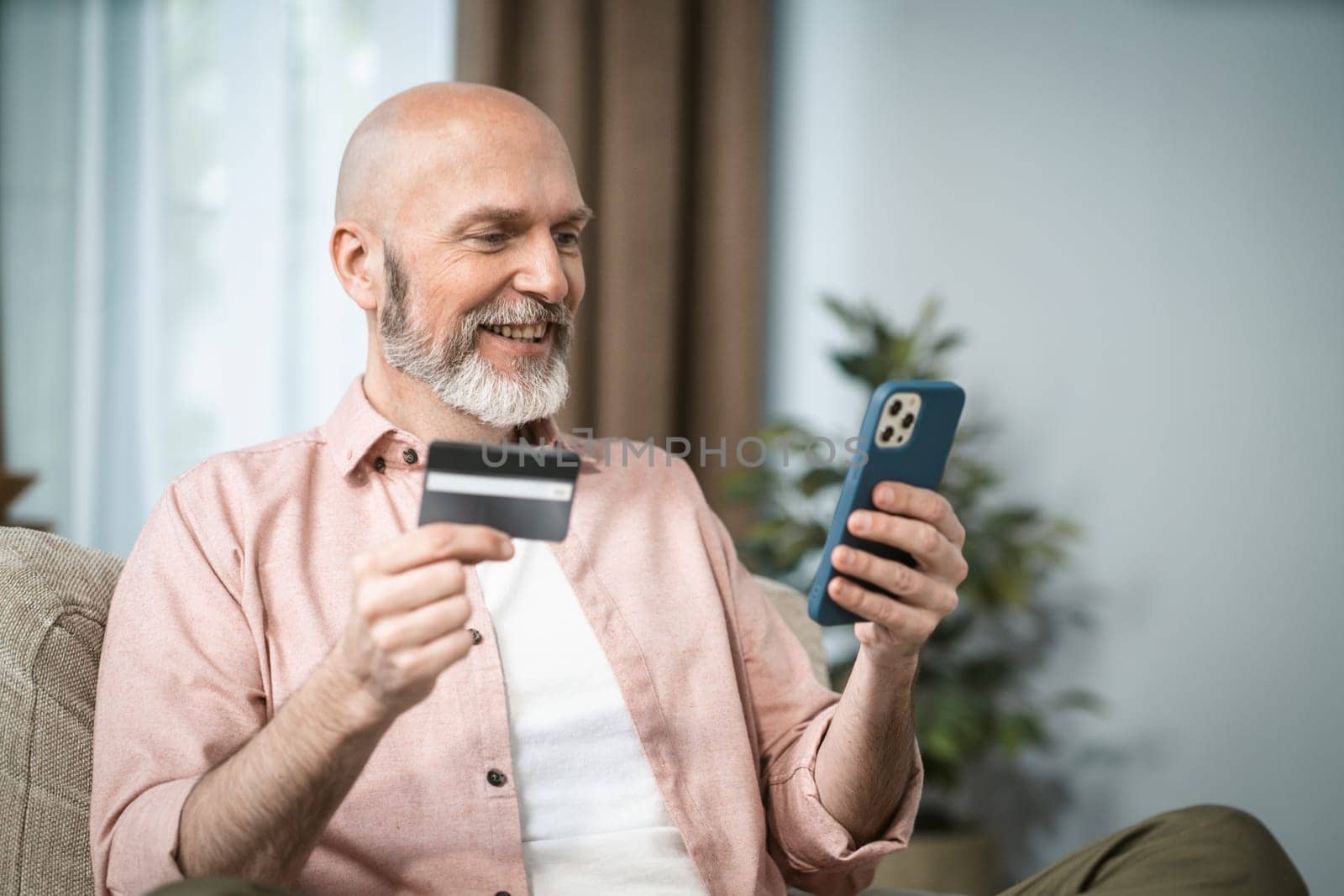 Senior man holds credit card in one hand and mobile phone in other. Convenience and accessibility of digital transactions for elderly, emphasizing their ability to adapt to modern technology. . High quality photo