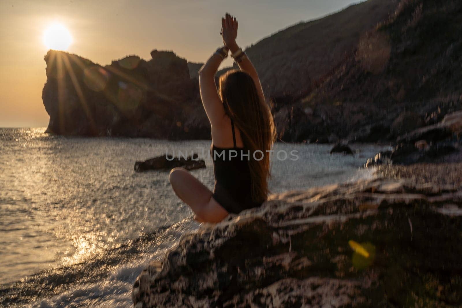 Woman tourist enjoying sunset over the sea mountain landscape. Sits outdoors on a rock above the sea. She is wearing jeans and a blue hoodie. Healthy lifestyle, harmony and meditation.