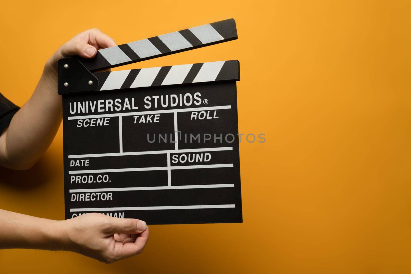 Hands holding black clapperboard on yellow background. Video production, film, cinema industry concept.