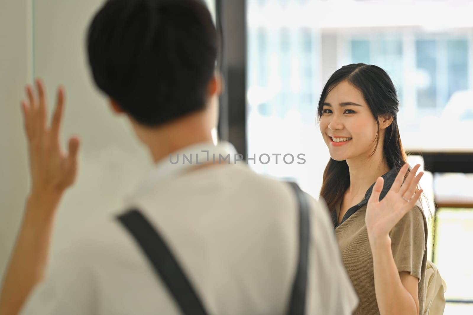 Friendly asian female college student waving hand while greeting her classmate. Education and youth lifestyle concept by prathanchorruangsak