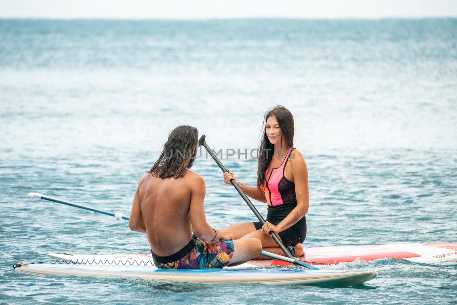 Sea woman and man on sup. Silhouette of happy young woman and man, surfing on SUP board, confident paddling through water surface. Idyllic sunset. Active lifestyle at sea or river