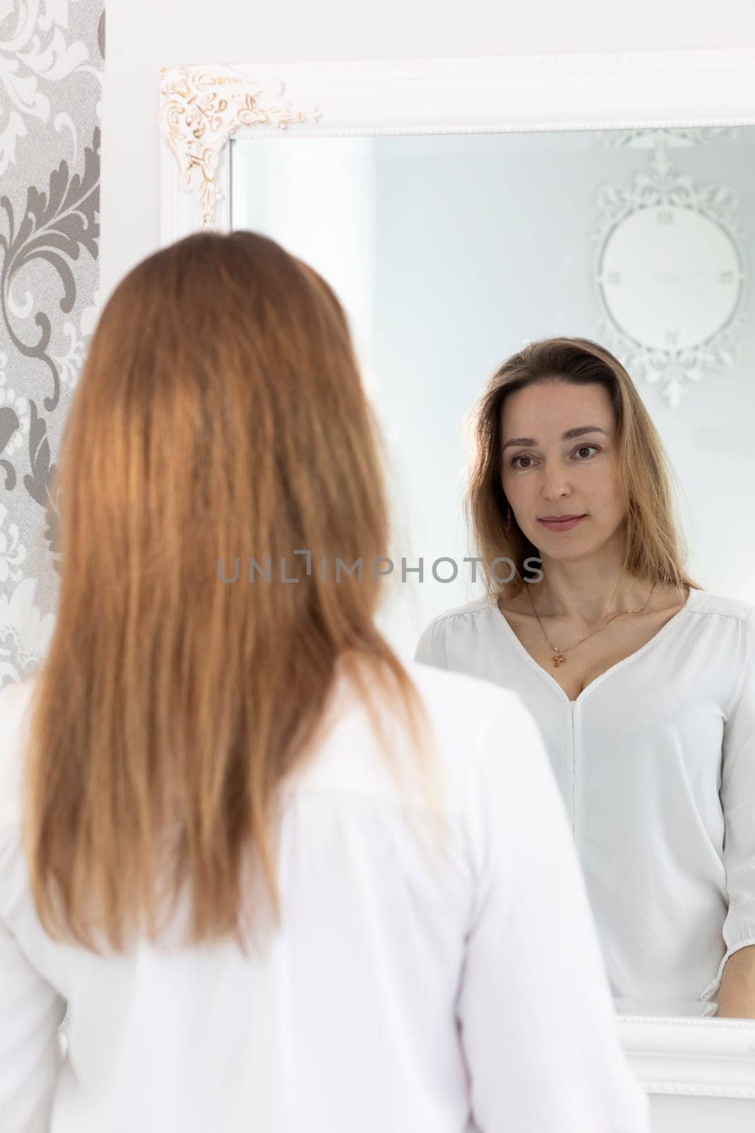 Portrait Of Charming Beautiful Brunette Caucasian 40 Yo Woman Looking At Mirror And Smiling. Healthy Moisturized Skin Care, Aging Beauty, Skincare Treatment Cosmetics Concept. Vertical Plane