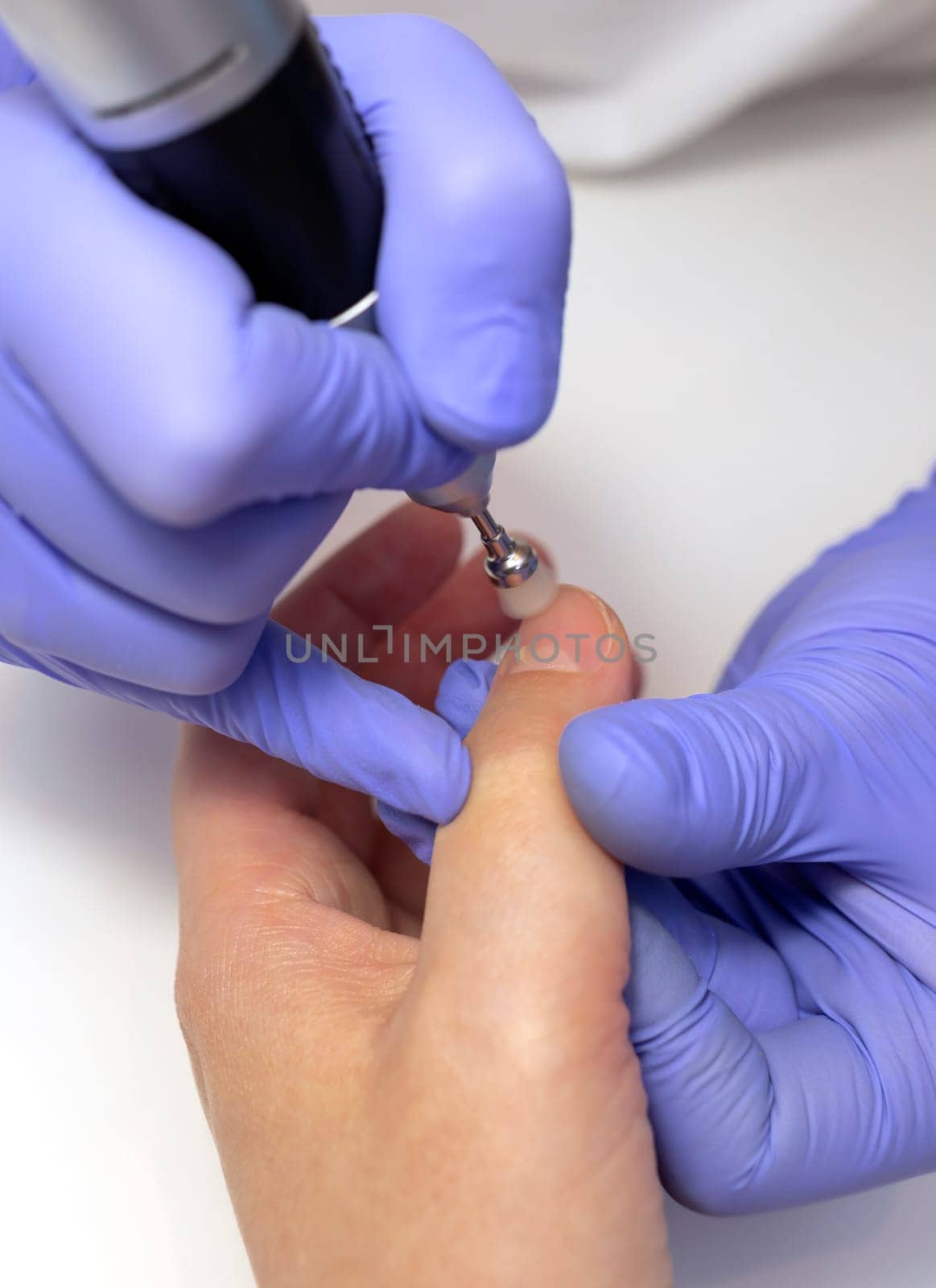 Nail beautician gloss client's fingernails by rubbing beeswax cream, paste or powder with minerals with soft nozzle of hardware nail file drill machine on work station in spa salon.Top view Vertical