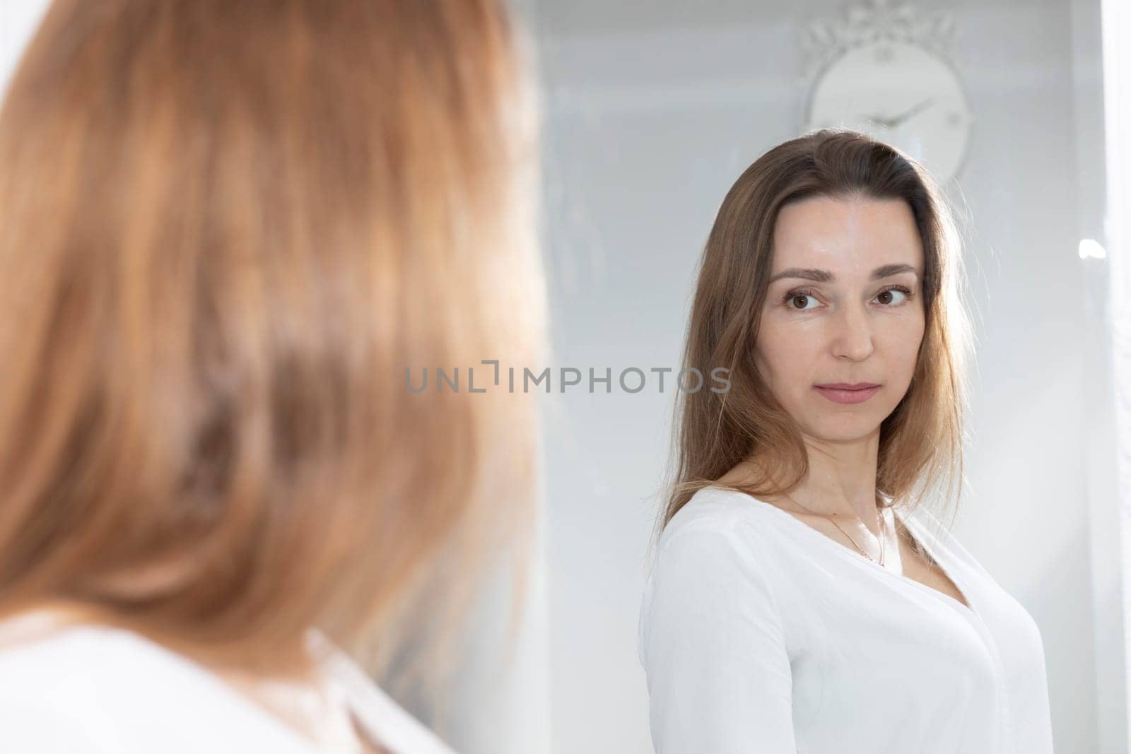Portrait Of Charming Beautiful Brunette Caucasian 40 Yo Woman Looking At Mirror And Smiling. Healthy Moisturized Skin Care, Aging Beauty, Skincare Treatment Cosmetics Concept. Horizontal Plane