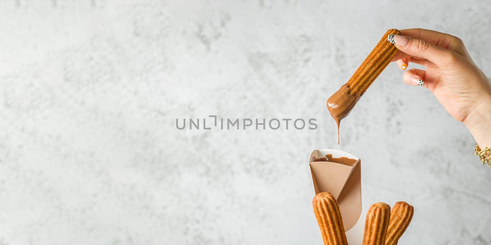Woman taking churros from a cone and dipping it in chocolate sauce by Sonat