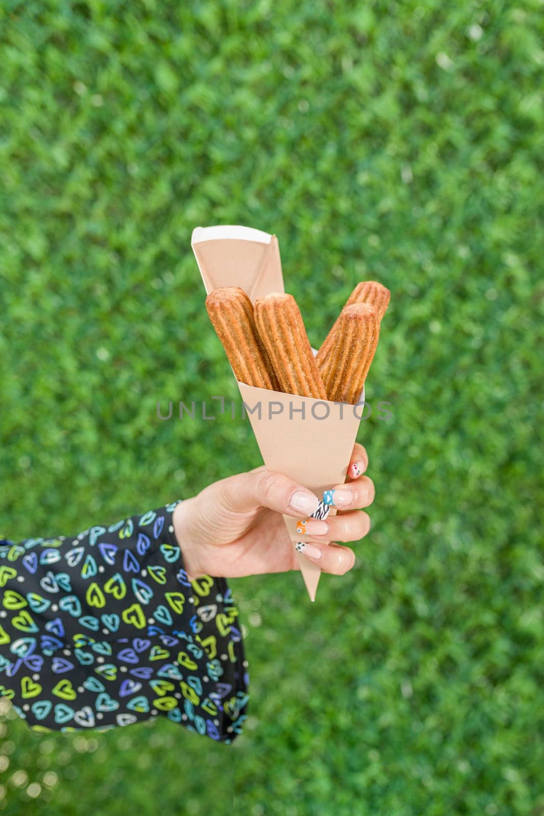 woman holding churros in cardboard box in front of green grass wall