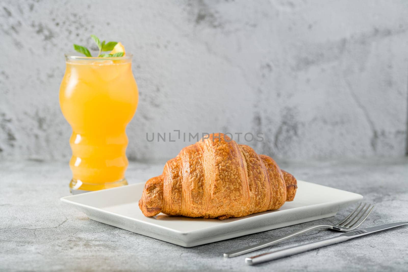 Croissant on a white porcelain plate with freshly squeezed orange juice on the side