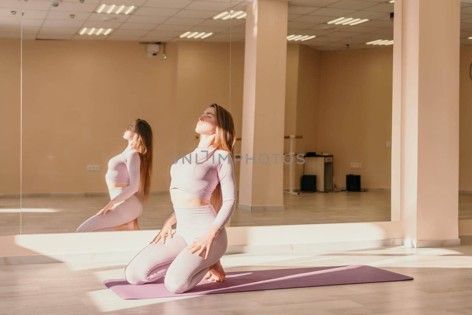 Young woman with long hair in white swimsuit and boho style braclets practicing outdoors on yoga mat by the sea on a sunset. Women's yoga fitness routine. Healthy lifestyle, harmony and meditation