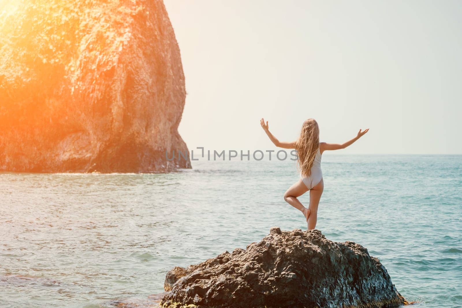 Woman and her daughter practicing balancing yoga pose on one leg up together on rock in the sea. Silhouette mother and daughter doing yoga at beach by panophotograph