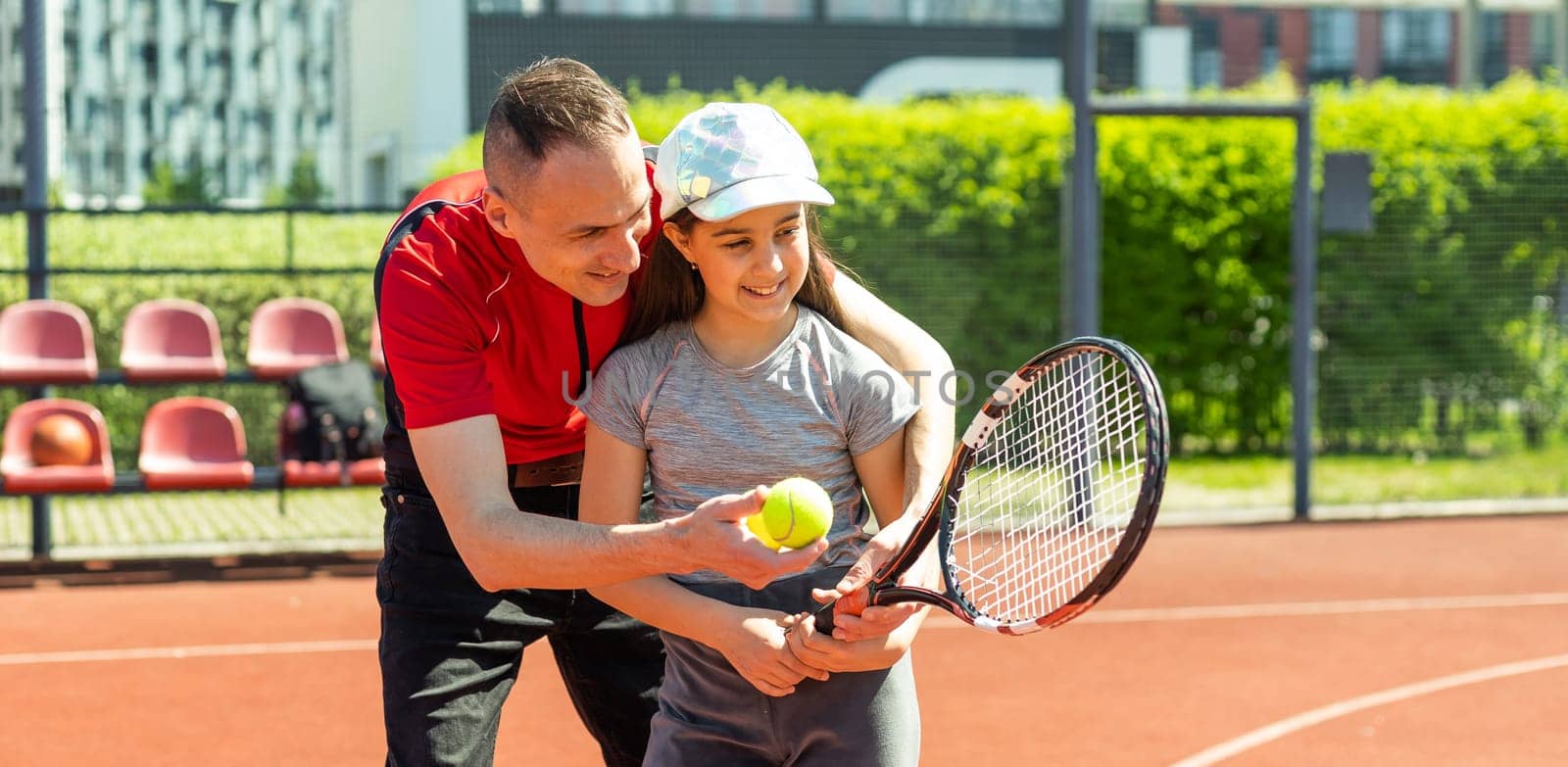 Father is a tennis coach for his daughter. Female child is playing in tandem with her daddy in doubles tennis.