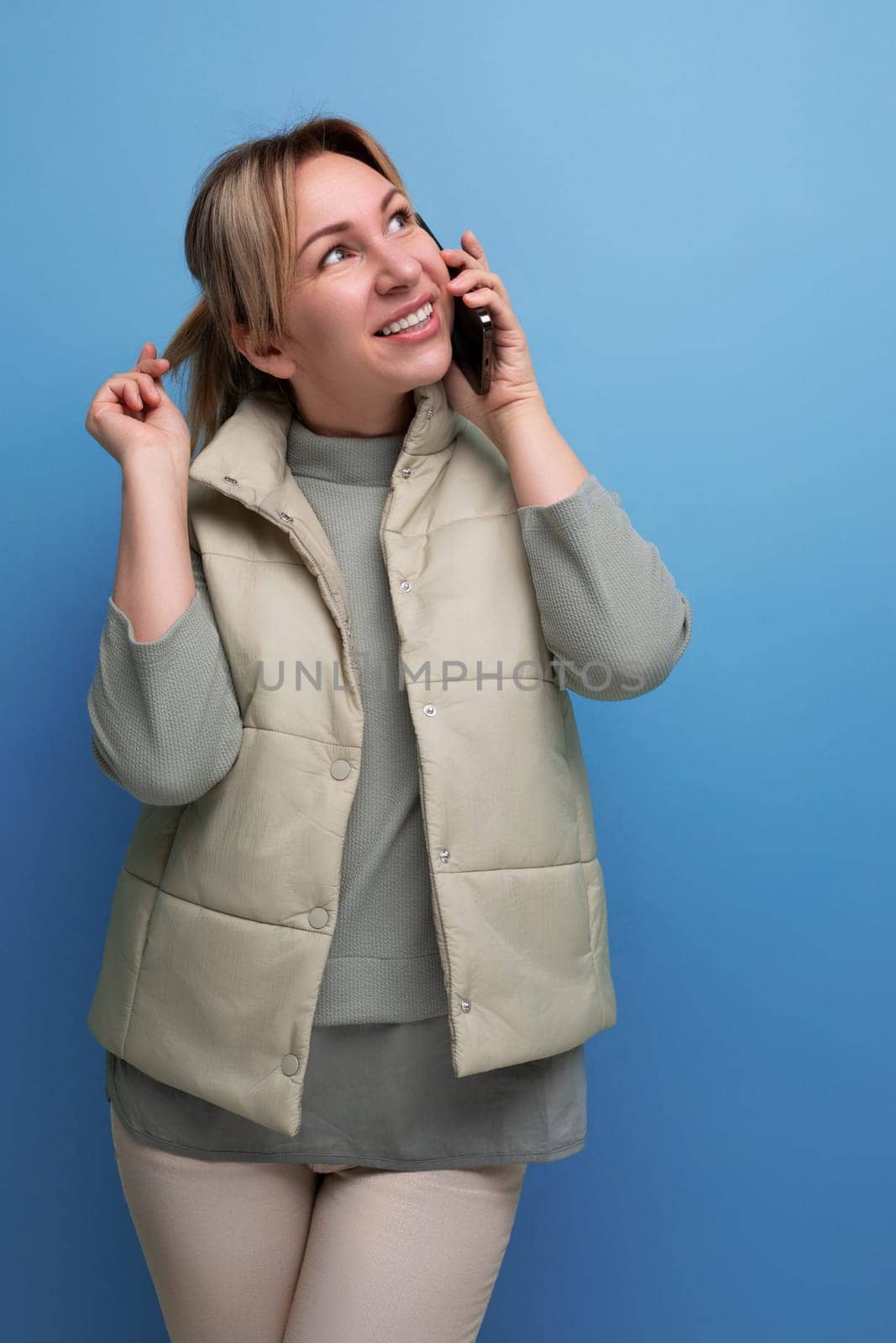 blond millennial woman talking on the phone on a blue isolated background.