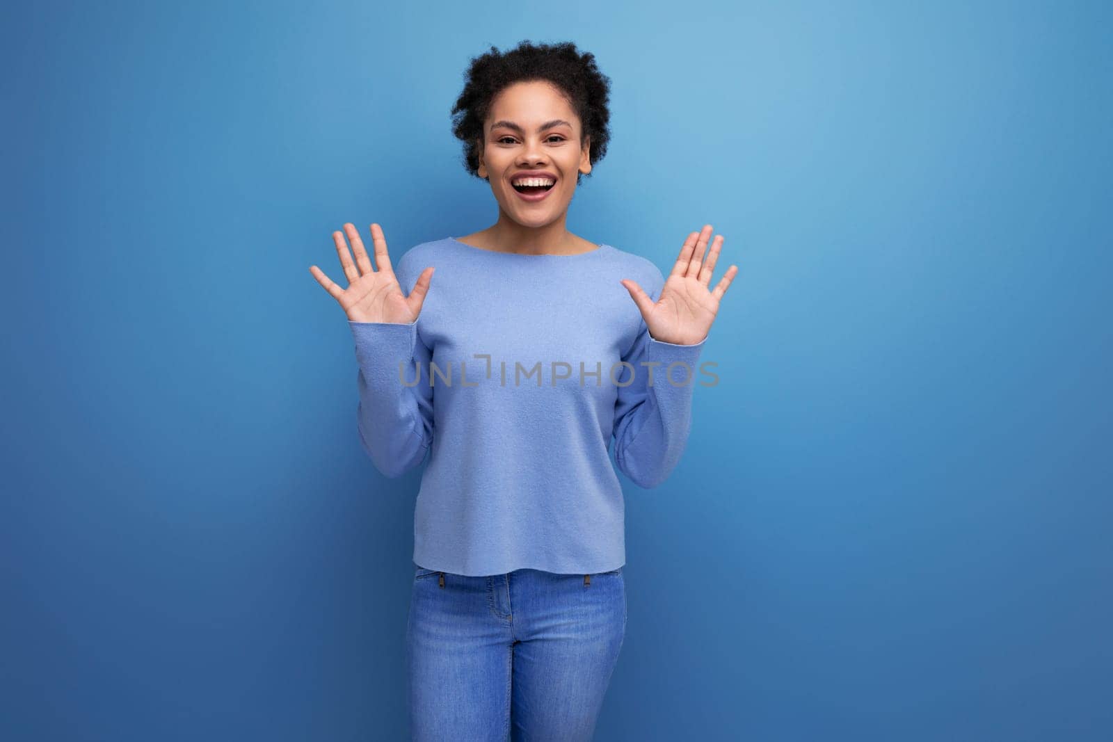 happy young latin 20s woman with black hair in a bun on blue background.