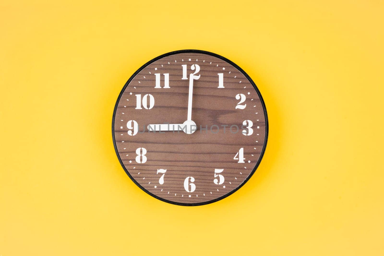 The Retro wooden clock at 9 O' clock on yellow color background. by Gamjai