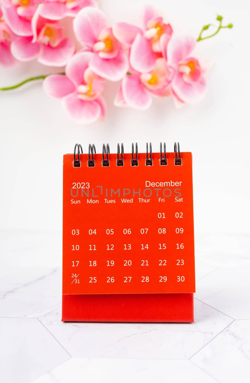 Red calendar December 2023. Desk calendar for year 2023 and pink orchid on marble background.